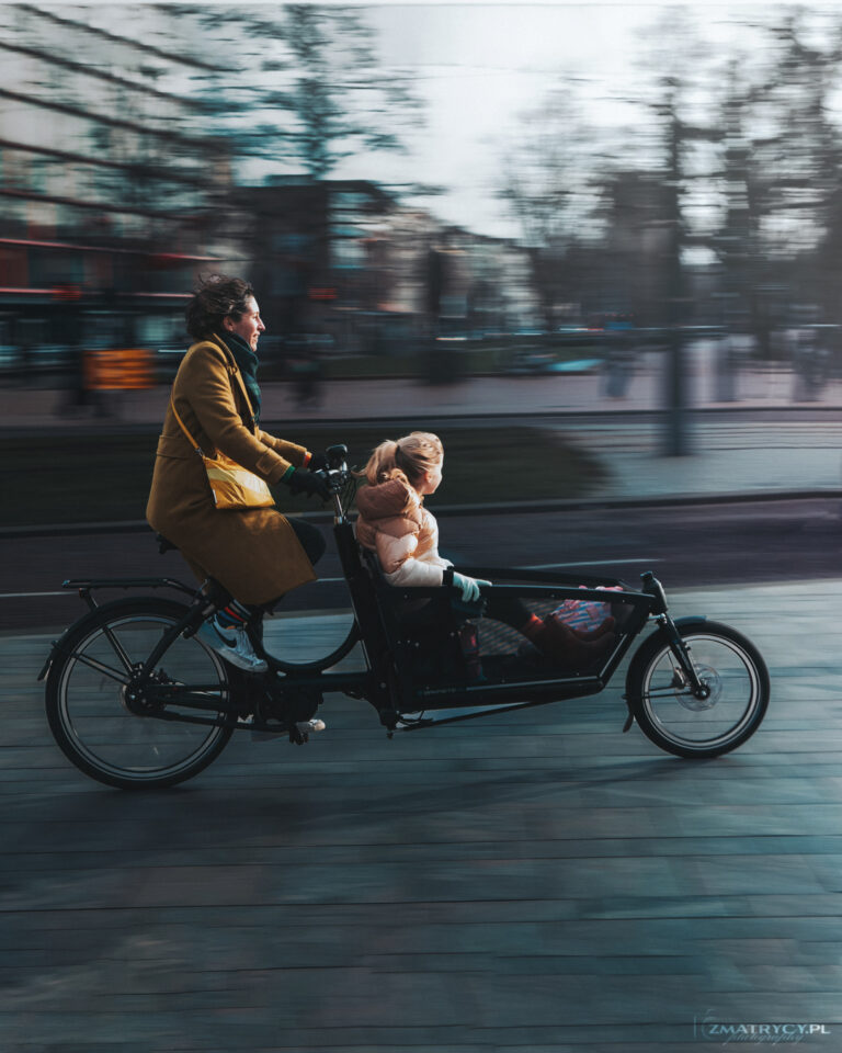 Osoba jadąca na rowerze z dzieckiem i rozmytym w poziomie ulicznym tłem