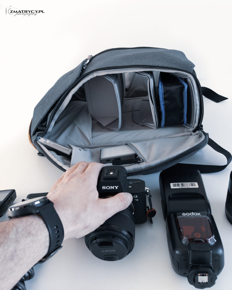Otwarty bok plecaka z przegrodami, obok aparat Sony i lampa Godox