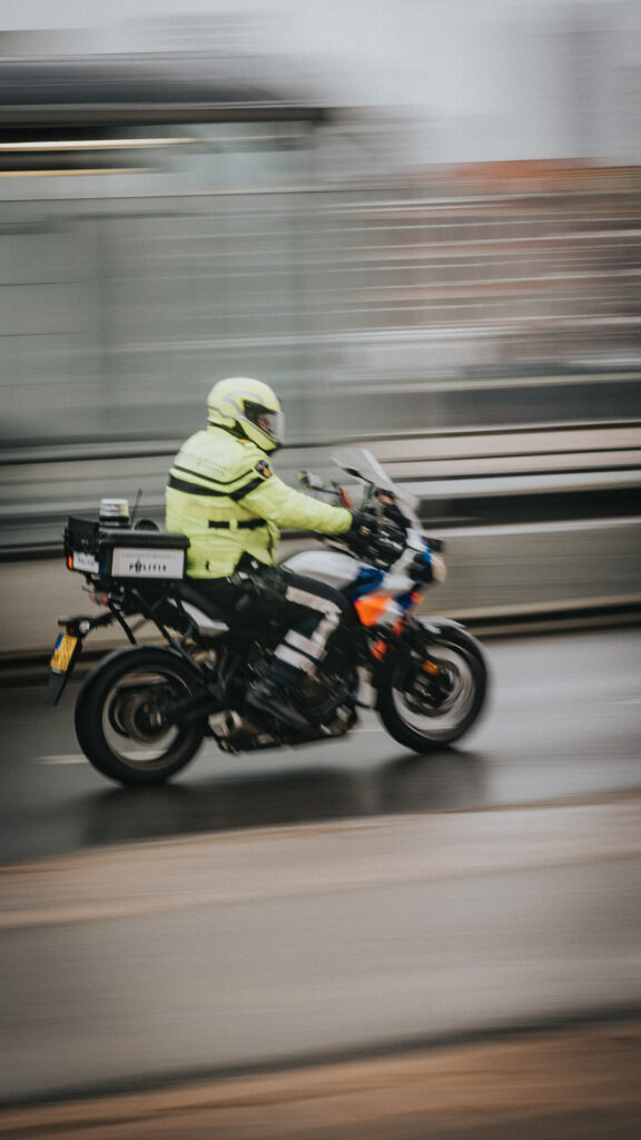 Motocyklista w jasnej kurtce na tle poziomych smug ruchu