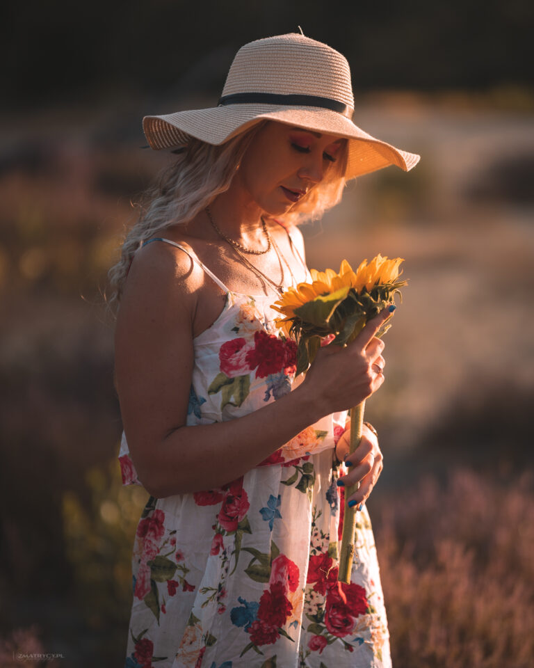 kobieta w sukience i kapeluszu patrzy w kwiat słonecznika