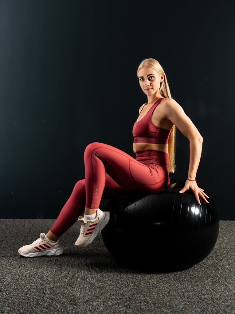 Model wearing a burgundy Innoni sports outfit seated on an exercise ball