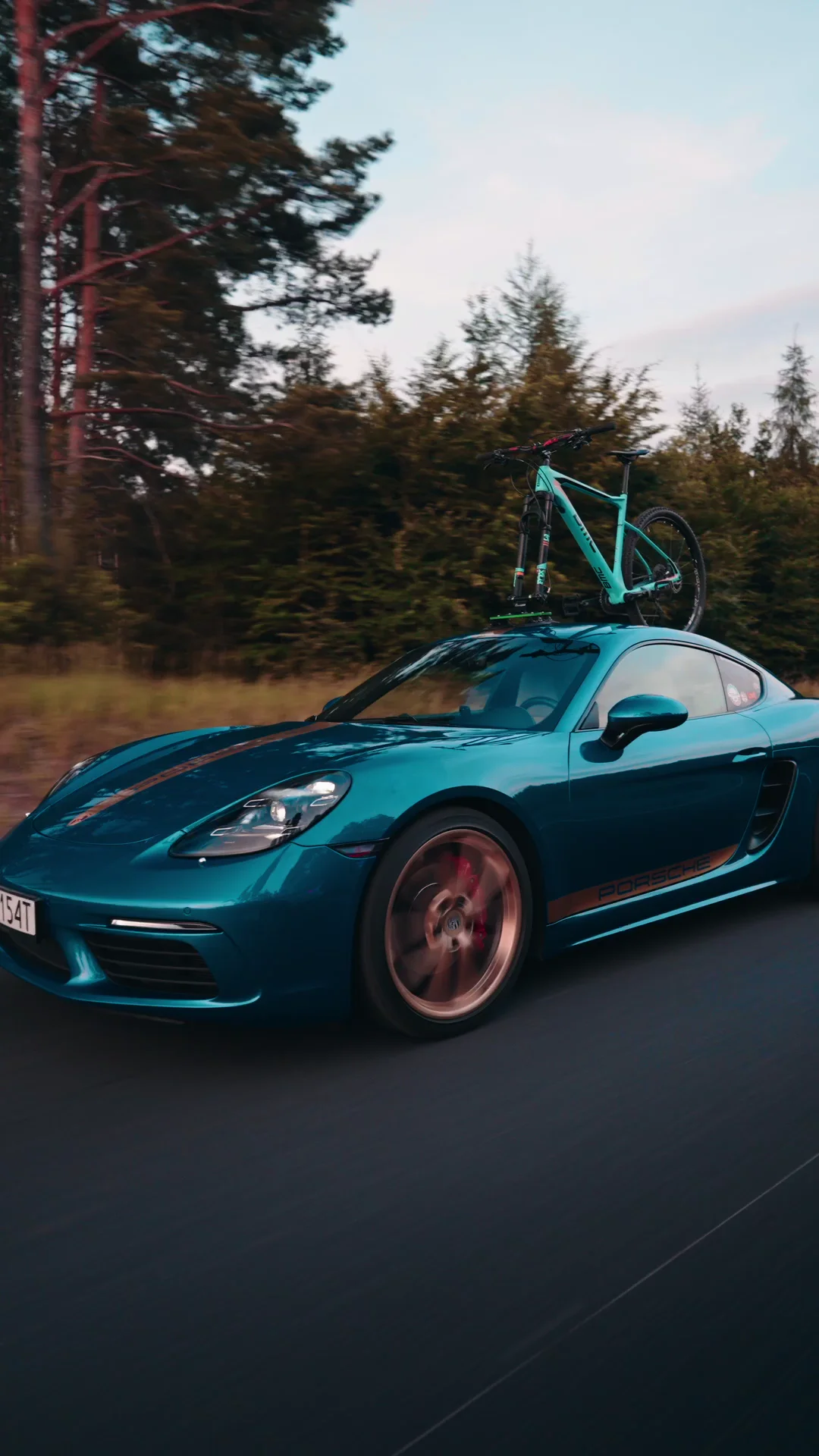 Turkusowe Porsche z rowerem na dachu podczas jazdy