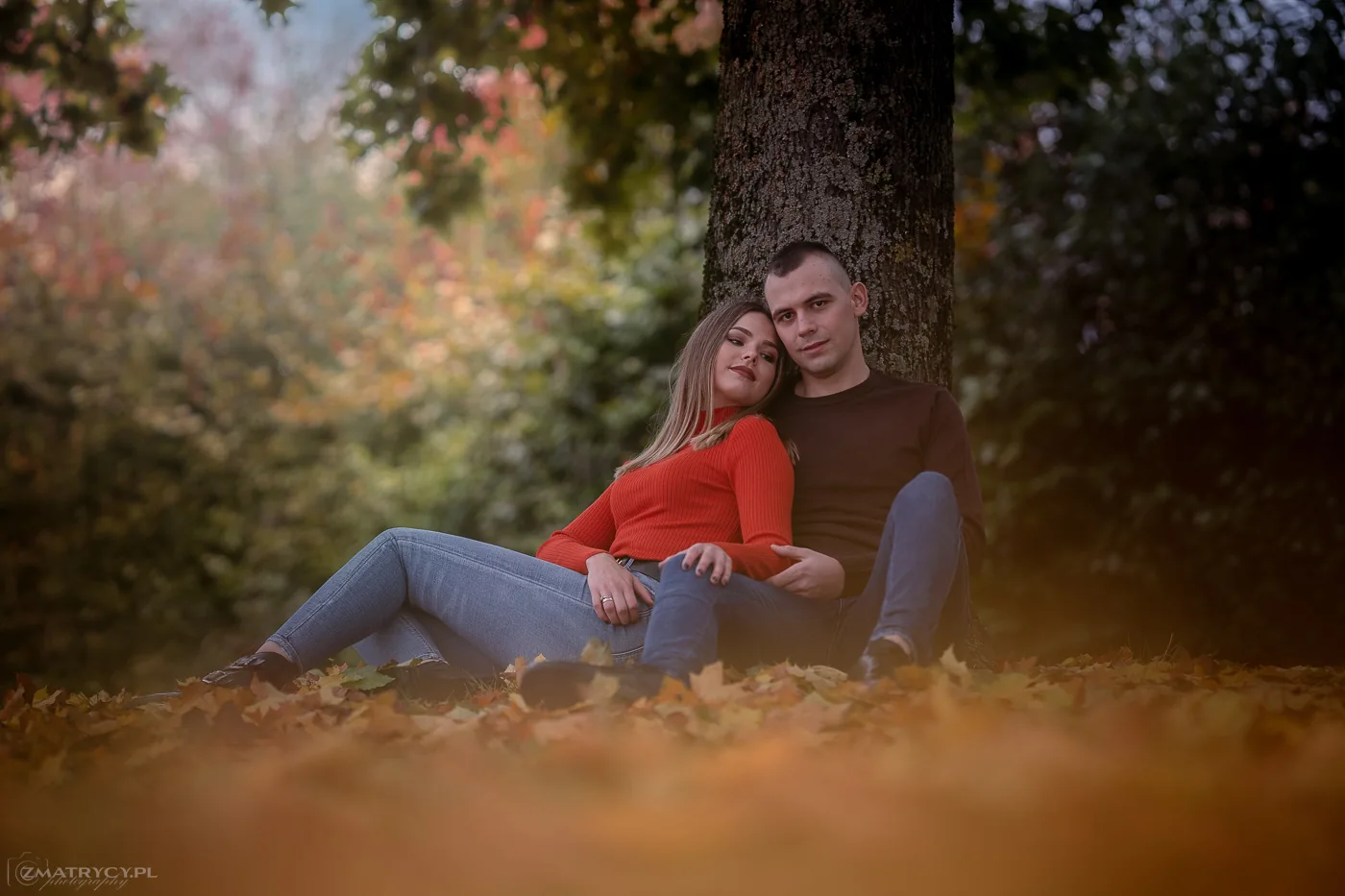 Paar sitzt gemeinsam an einem Baum im Herbst